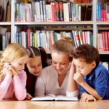 Portrait of pupils and teacher looking at page of interesting book in library